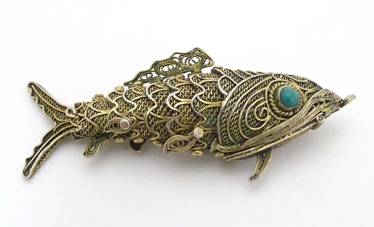 A silver gilt pendant formed as an articulated fish with green stone eyes hinging open to reveal
