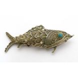 A silver gilt pendant formed as an articulated fish with green stone eyes hinging open to reveal