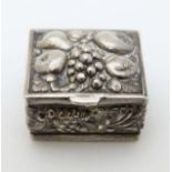 A silver pill box of squared form with fruit decoration.