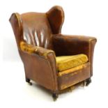 An early 20thC wingback club armchair with leather upholstery adorned with brass studs,