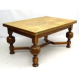 An early 20thC oak draw leaf dining table standing on large cup and cover legs,