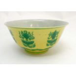 A Chinese bowl decorated with green auspicious items above a lotus flower head and scroll to yellow