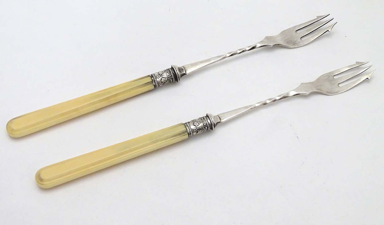 A pair of silver pickle forks with ivory handles.