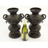 A pair of Oriental patinated bronze sensor / vases with dragon handles and decorated with raptors