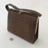 A Ladies brown crocodile handbag with gilt coloured hardware, and pale faux leather interior.