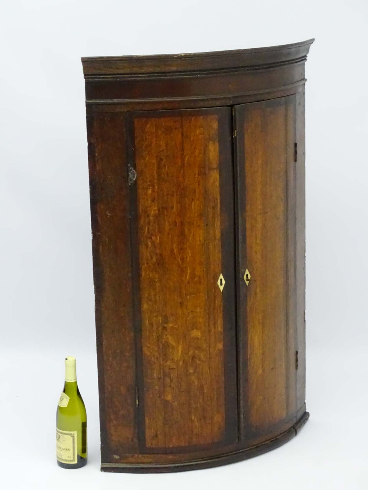 A late 18thC oak bow fronted corner cupboard with mahogany cross banded doors and mahogany frieze