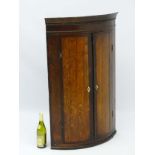 A late 18thC oak bow fronted corner cupboard with mahogany cross banded doors and mahogany frieze