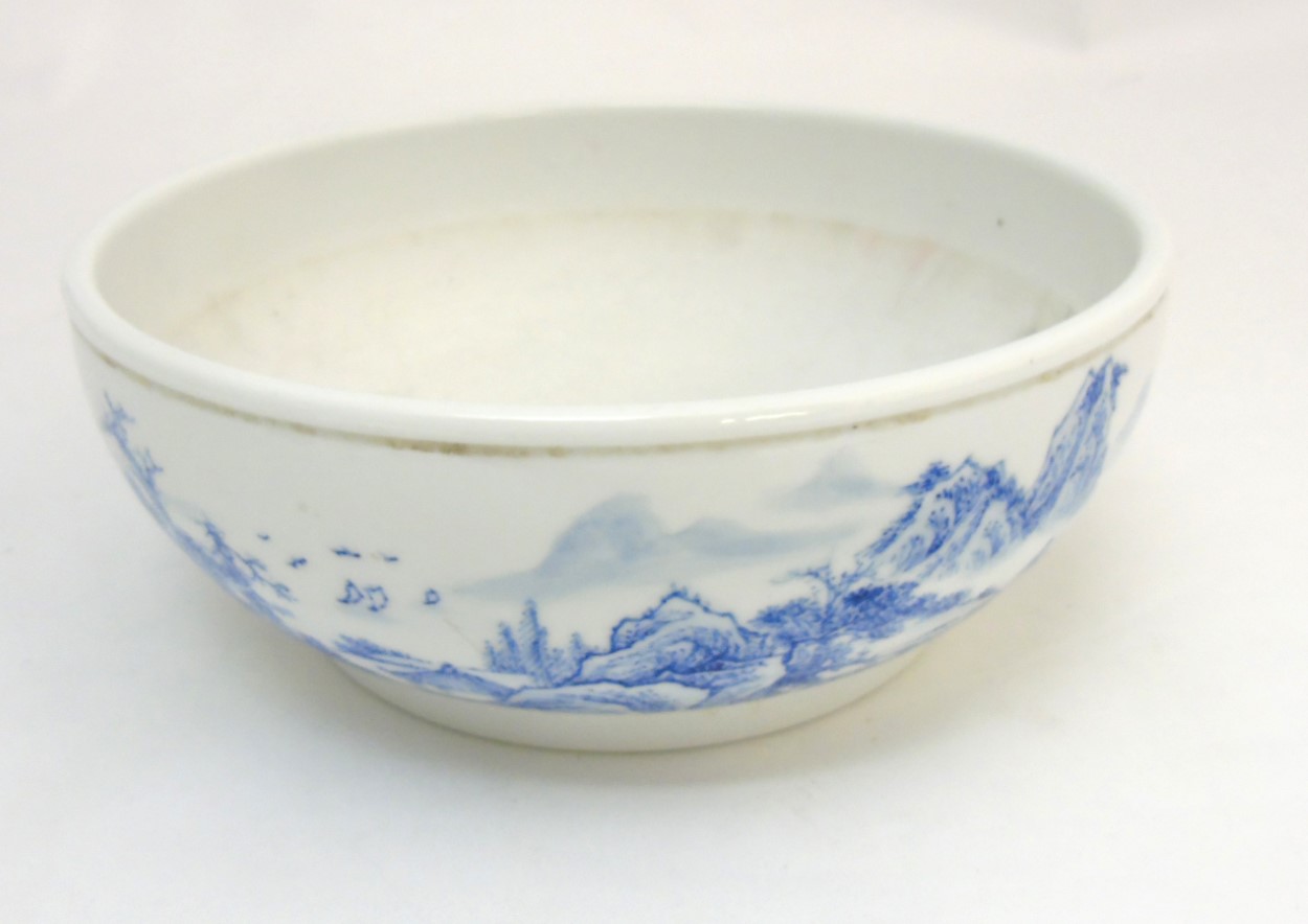 A Chinese blue and white bowl decorated in an underglaze blue continuous landscape and iron red