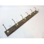 A set of 6 Victorian brass coat hooks with porcelain ends on a wooden mount.