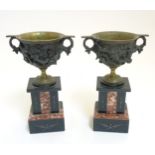 A pair of cast bronze pedestal cup urns on slate and marble bases.