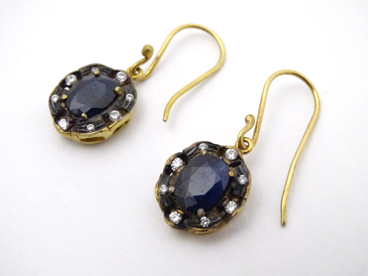 A pair of yellow metal drop earrings set with blue and white stones.