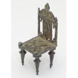A white metal miniature model of a chair with filigree decoration. possibly Persian.