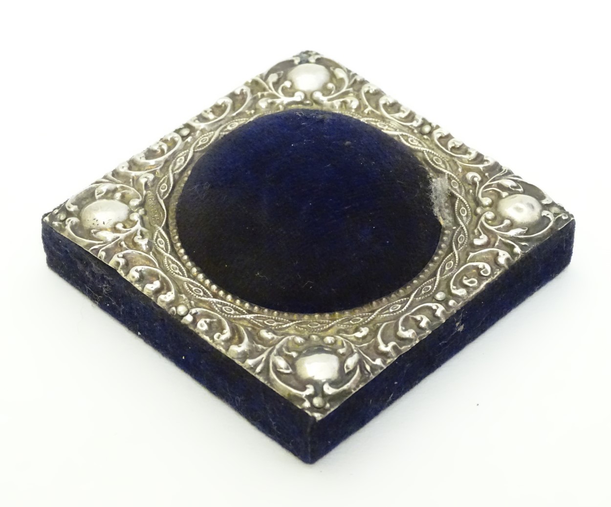 A blue velvet hat pin / pin cushion of squared form with domed centre and having embossed silver