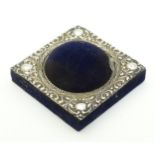 A blue velvet hat pin / pin cushion of squared form with domed centre and having embossed silver