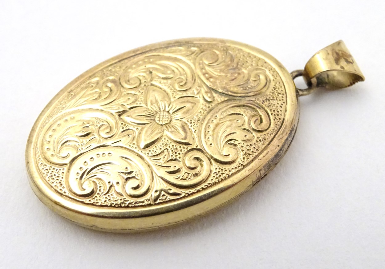 A yellow metal locket of oval form with floral and C-scroll decoration approx 1 1/4" long