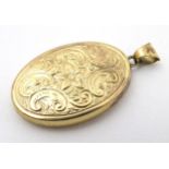 A yellow metal locket of oval form with floral and C-scroll decoration approx 1 1/4" long