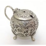 A white metal mustard pot of spherical forms with floral and acanthus scroll decoration.