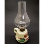 A small glass oil lamp with floral decoration, loop handle and clear glass chimney.