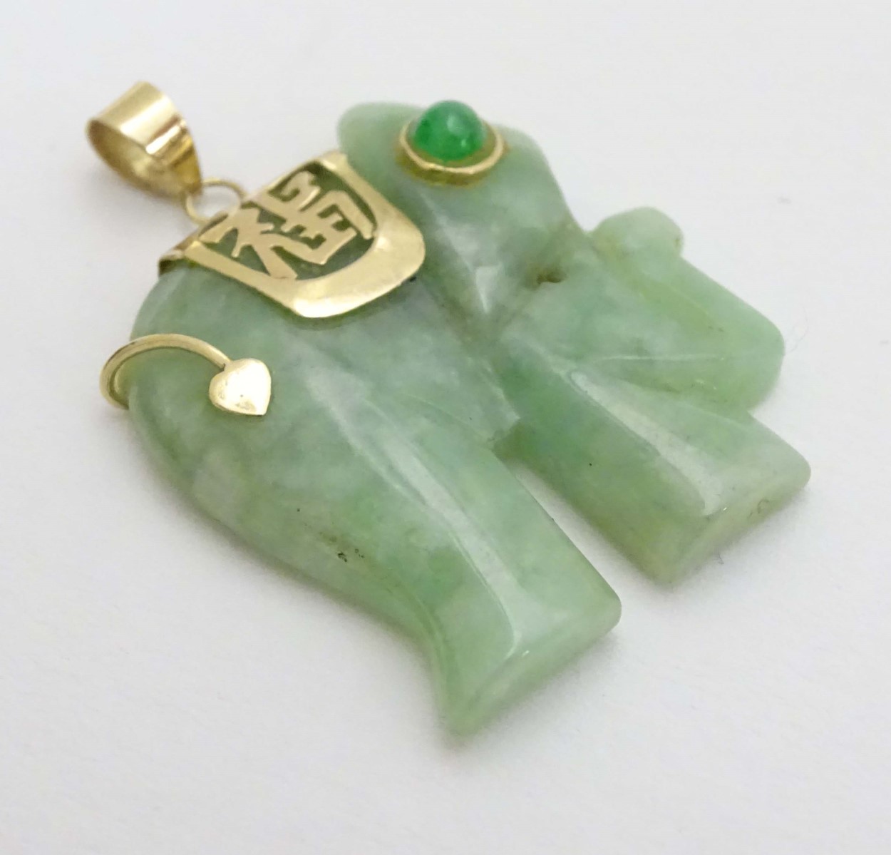 A carved jade pendant formed as a elephant with jade cabochon eye and 14kt gold mounts.