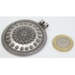 A large silver pendant of circular form with geometric decoration.