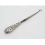 A silver handled button hook with embossed fruiting vine decoration.