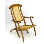A late 19thC / early 20thC folding steamer chair with bowed top rail and caned backrest and seat,