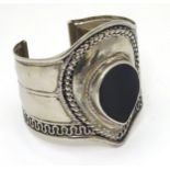 A white metal bangle of cuff form set with black enamel detail.