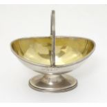 A silver table salt / bonbon formed as a pedestal basket with swing handle and gilded interior.
