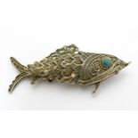 A silver gilt pendant formed as an articulated fish with green stone eyes hinging open to reveal