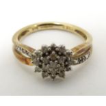 A 9ct gold ring set with diamond cluster flanked by diamonds to shoulders.