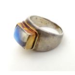 A white metal ring set with moonstone cabochon in a yellow metal setting.