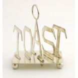 A silver plate toast rack, the divisions formed as letters spelling ' TOAST'.