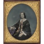 *Sixth-plate tinted ambrotype of a woman seated by a table, by George Coulder, 1850s, gilt