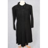 A BLACK UTILITY LONG SLEEVE DAY DRESS, the bodice with front button fastening, the skirt falling