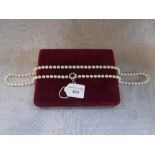 A CULTURED PEARL NECKLACE with a 9ct yellow gold clasp, decorated with pearls and a gemstone, in a