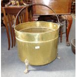 A LARGE BRASS LOG BIN on hairy paw feet, with an iron swing handle, 48 cm dia.