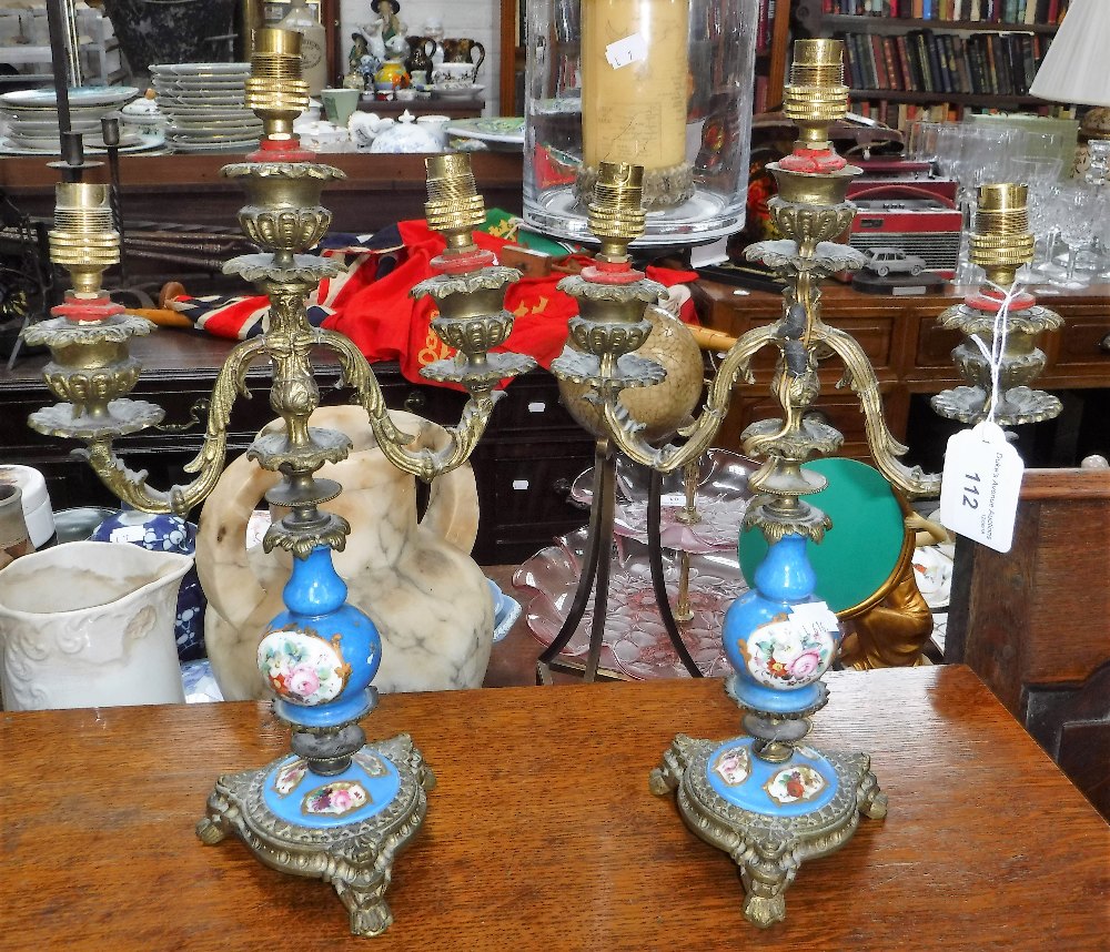 A PAIR OF CONTINENTAL BRASS CANDELABRA with blue and floral ceramic centres (drilled and converted