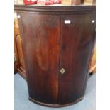 A GEORGE III MAHOGANY BOWFRONTED HANGING CORNER CUPBOARD with green painted inte
