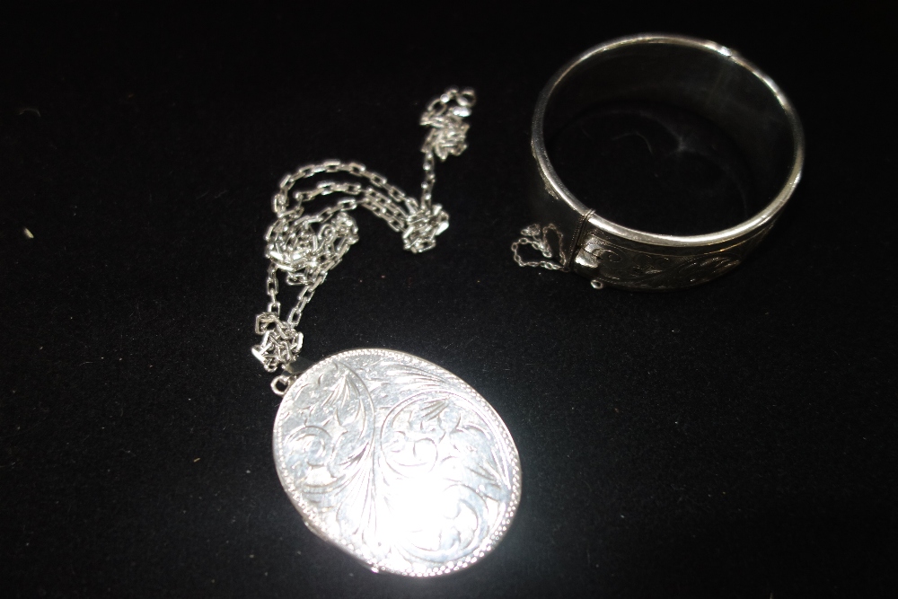 A SILVER BANGLE and a locket attached to a silver chain