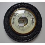 A 19TH CENTURY ANEROID BAROMETER in carved and ebonised circular frame
