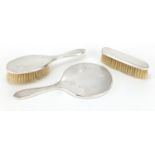 Three silver backed vanity items, with engine turned decoration, hand mirror, hair brush and clothes