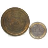 Two Islamic brass trays, one with silver inlay, both decorated and engraved with panels of script,