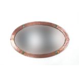 Oval Arts & Crafts beaten copper mirror, set with four green cabochons with bevelled glass, 89cm x