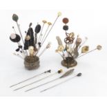 Victorian and later hatpins arranged in two hatpin stands, one being silver embossed with foliage,