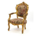 Ornate French gilt wood open armchair with floral upholstery, carved with rosettes and scrolls,