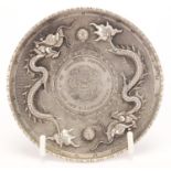 Chinese silver coloured metal coin design dish, embossed with two dragons chasing a flaming pearl,