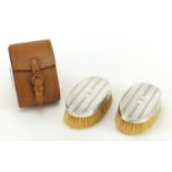 Pair of silver backed clothes brushes with engine turned decoration and leather case, D M Co