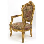 Ornate French gilt wood open armchair with floral upholstery, carved with rosettes and scrolls,