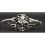 A sterling silver bangle bracelet in the form of two arms holding a skull. Weighs 38.6 grams