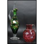 A 19th century cranberry glass jug handpainted overlay of flowers together with a green glass